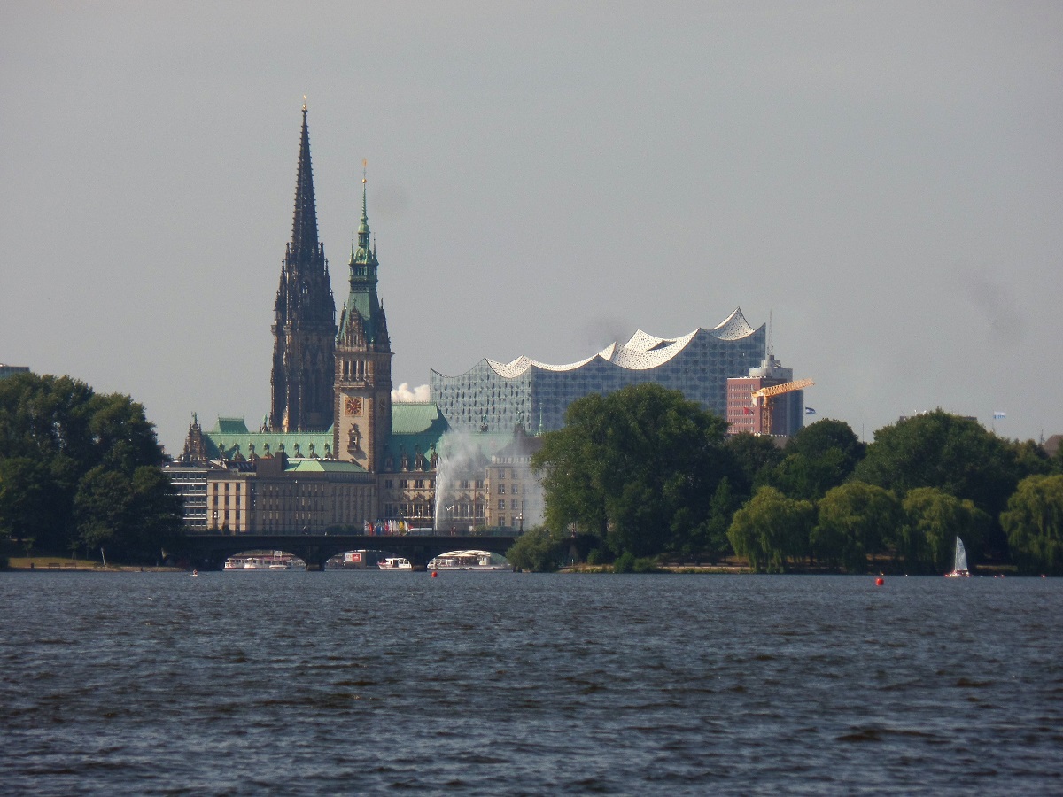 Hamburg am 28.7.2018: Blick ber die Auenalster mit den Bgen der Lombardsbrcke, der Fontne auf der Binnenalster, den Trmen von St. Nikolai und Rathaus und die Elbphilharmonie im Frhdunst der Stadt /