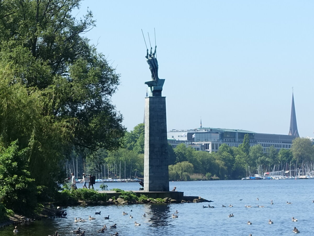 Hamburg am 30.5.2021: auf der hohen Stele die Skulptur „Drei Mnner im Boot“, 1952/53 erschaffen von Edwin Paul Scharff, in Erinnerung an drei Gefallene im Zweiten Weltkrieg, die auf einer Flakbatterie vor diesem Alsterufer eingesetzt waren.