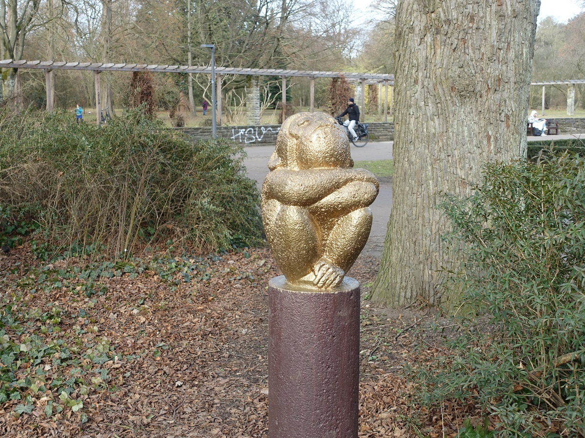 Hamburg, an den Rosengrten im Stadtpark (Winterhude), am 25.2.2021: Skulptur „Hockender Affe“  auf einer Stele, ca. 1955 von Hans-Peter Feddersen aus Muschelkalk erschaffen, irgendwer hat ihn mit Bronzefarbe „verschlimmbessert“   /