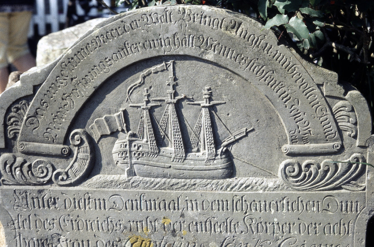 Historisches Grabstein am St. Clemens Friedhof auf der Insel Amrum. Bild vom Dia. Aufnahme: August 1999.  Die Grabsteine auf der Insel Amrum werden auch sprechende Grabsteine genannt, da die in den Stein gemeielten Inschriften aus dem Leben der Verstorbenen berichten.