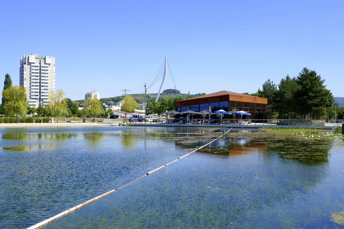 Lahr, Blick von der Brcke ber den Stegmattensee auf das Restaurant  Haus am See , dahinter der 50m hohe Pylon der Fu-und Radweg Brcke, alles errichtet zur Landesgartenschau 2018, Aug.2022