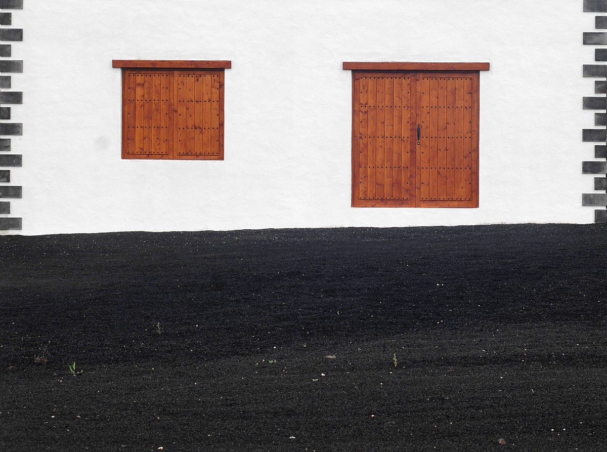 Lanzarote - Hausfassade mit schwarzen Lava-Sand im Vordergrund. Aufnahme: Juli 2009.