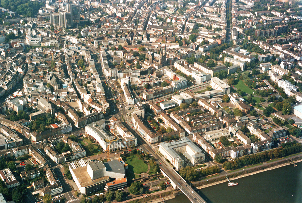 Luftaufnahme von Bonn 1992. Unten Kennedybrcke ber den Rhein, in Verlngerung Bertha-von-Suttner-Platz und Stadthaus (Hochhaus), Mitte rechts die  Stiftskirche . Mitte links die  Stiftung Namen Jesu Kirche . Am Brckenende links das  Theater Bonn  und rechts das  Hilton-Bonn .