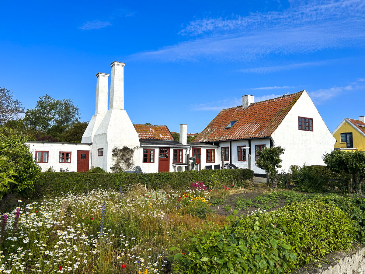 Rucherei in Gudhjem - Die Ruchereien auf Bornholm spiegeln Tradition und Seele der dnischen Insel wieder. Ihre Schornsteine sind in fast jedem Ort zu sehen und bestimmen das Bild. Auch wenn die Heringe heute nicht mehr aus der Ostsee rund um Bornholm kommen, ist der goldfarbene gerucherte Hering die kulinarische Bornholmer Spezialitt. 
Aufnahme: 16. Juni 2023.