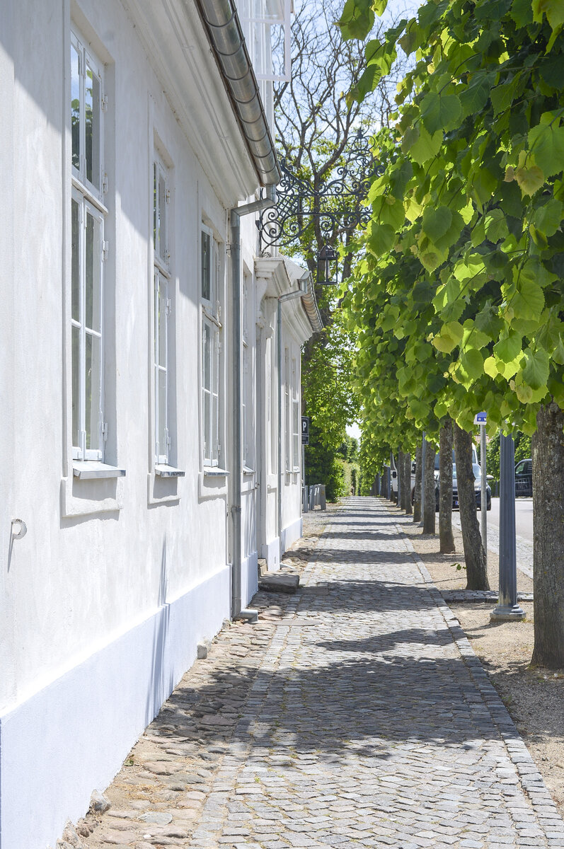 Wei gestrichenes Haus und Brgersteig in der Slotsgade (deutsch Schlostrae) in Fredensborg auf Seeland. Aufnahme: 24. Juni 2023.