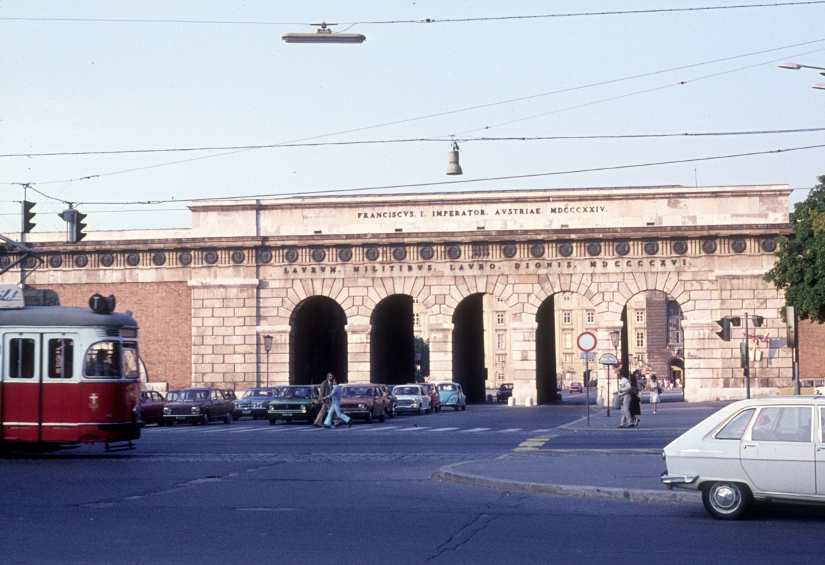 Wien im Juli 1975. Das ussere Burgtor vom Burgring gesehen. - Das Tor wurde am 16. Oktober 1824 erffnet. Die obere Inschrift  Franciscus I Imperator Austriae MDCCCXXIV  (: Franz der Erste, Kaiser von sterreich, 1924) zeigt auf die Regierungszeit des Kaisers Franz des Ersten und das Erffnungsjahr, whrend die untere Inschrift, die vom Jahre 1916 stammt, den Soldaten, die fr sterreich und Deutschland in den Jahren 1914 - 1916 gekmpft hatten, gewidmet ist. Der Text dieser Inschrift lautet folgendermassen  Laurum militibus lauro dignis MDCCCCXVI  (: (einen)Lorbeerkranz den Soldaten, die der Lorbeere wrdig sind, 1916). 