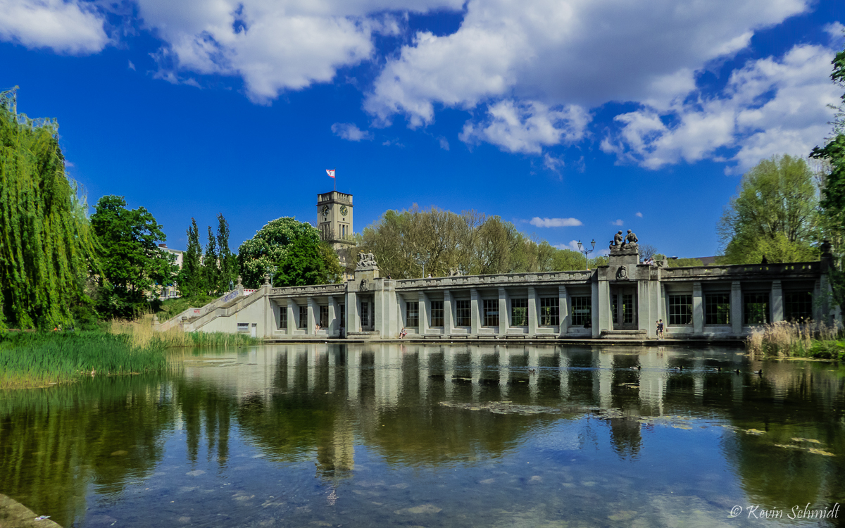 Wir befinden uns in Berlin-Schneberg westlich des U-Bahnhofs Rathaus Schneberg, den wir hier von auen einmal quasi im Original und einmal im Wasser gespiegelt sehen, im Rudolph-Wilde-Park, dem Schneberger Teil des langen Parkstreifens, der sich weiter westlich als Volkspark Wilmersdorf fortsetzt. Der Tunnel der U-Bahn-Linie U4 erblickt hier lediglich ber die Lnge des Bahnhofs das Tageslicht. Im Hintergrund ist der Turm des Schneberger Rathauses, dem ehemaligen West-Berliner Sitz des Regierenden Brgermeisters, zu sehen, vor dem John F. Kennedy 1963 seine berhmte  Ich bin ein Berliner -Rede hielt. (08.05.2016)