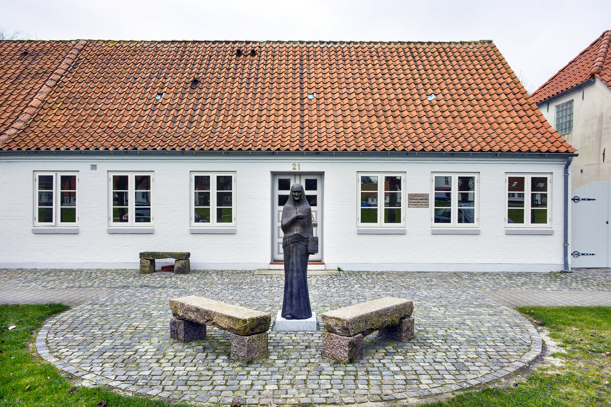Zur Erinnerung an Lgumklosters frhere Wohltterin Stinne mit der Bibel (Kjestine Andersen) steht eine Bronzefigur vor ihrem Haus an der Vestergade in der nordschleswigschen Kleinstadt. Aufnahme: 18. Mrz 2024.