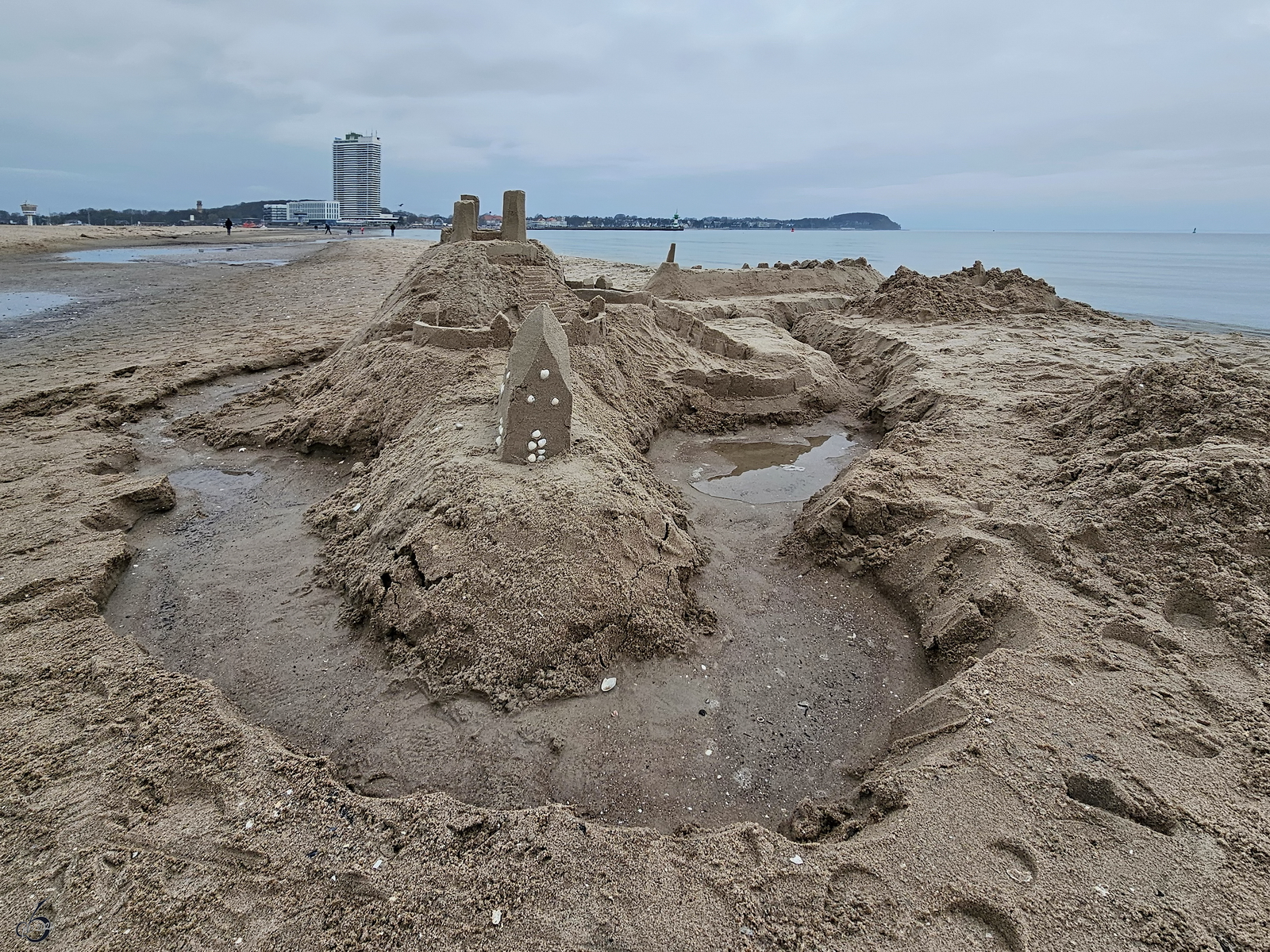 Blick auf eine Sandburg auf dem Priwall, im Hintergrund die markante Strandpromenade von Travemnde. (April 2024)