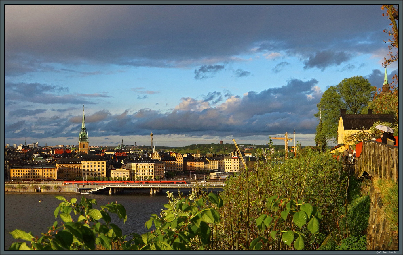 Der Monteliusvgen entlang des Mariaberget im Stadtteil Sdra bietet einen guten Blick ber die Innenstadt von Stockholm. Nach einem Regenschauer taucht die Sonne die Huser der Altstadt in leuchtendes Abendlicht. Heraus sticht der Turm der Deutschen Kirche St. Gertrud (Tystka kyrkan). (Stockholm, 17.05.2023)