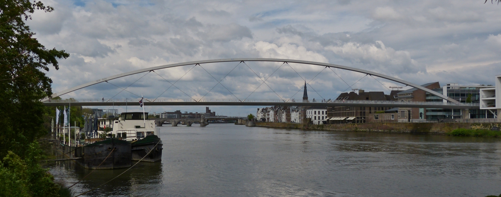 Die Fugnger- und Fahrradbrcke ber die Maas in Maastricht, links im Bild sieht man das Botelschiff was fest am Ufer verankert ist. 05.2023 
