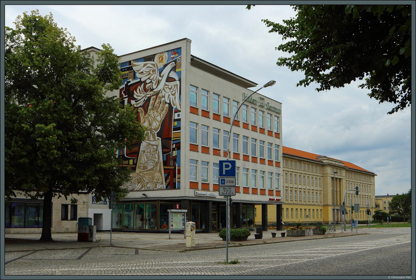 Die Lindenallee (ehemals Leninallee) im WK IV entstand Ende der 1950er Jahre und orientierte sich an der internationalen Moderne. Das ehemalige Kaufhaus Magnet trgt heute den Namen Linden-Zentrum. An seiner Seite befindet sich das Wandmosaik  Gemeinschaftsarbeit der sozialistischen Lnder  von 1963. Rechts ist das Rathaus zu sehen. (Eisenhttenstadt, 05.08.2023)