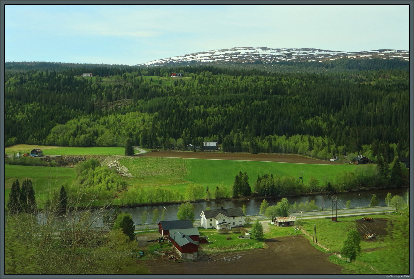 Entlang dem Fluss Gaula reihen sich mehrere Gehfte des Ortes Haltdalen. Im Hintergrund ist der 956 m hohe Berg Grmerra zu sehen, der auch am 27.05.2023 hoch teilweise schneebedeckt ist.