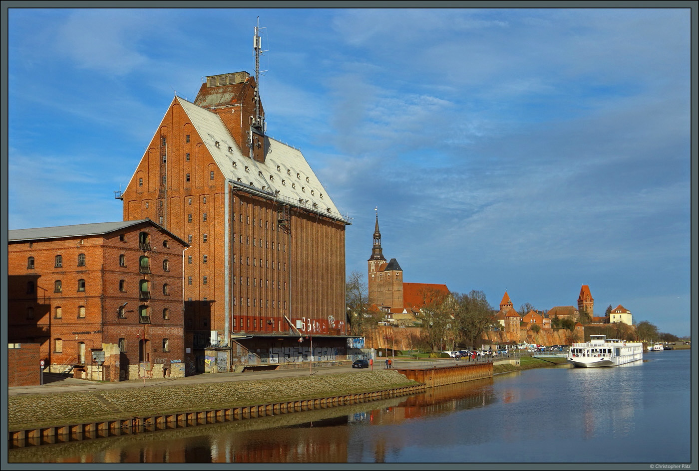 Zahlreiche Backsteinbauten prgen den Hafen von Tangermnde. Vorn sind zwei Speicher zu sehen, rechts davon die Kirche St. Stephan und die davor befindliche Stadtmauer. Am rechten Rand befindet sich die Burg Tangermnde. Im Hafen liegt am 05.02.2023 ein Flusskreuzfahrtschiff vor Anker.