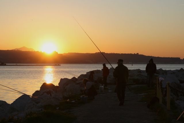 Angler stehen beim Sonnenuntergang auf der Hafenmole.
