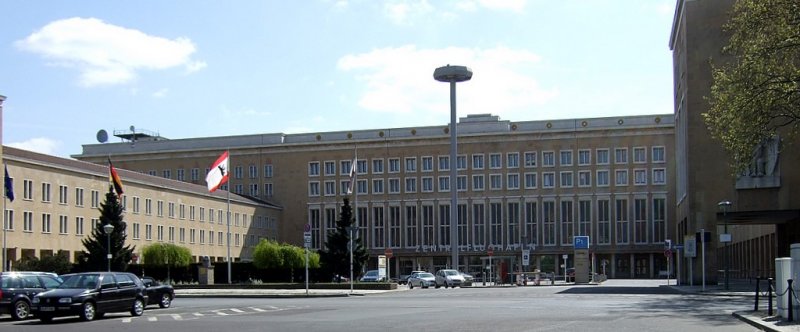 Berliner Architektur 1933-45: Flughafen Tempelhof. 1935 wurde er zum zentralen deutschen Luftkreuz ausgebaut. Sagebiel entwarf die riesige Anlage, die fr die Zeit viel zu berdimensioniert war. Um den Vorplatz legen sich Verwaltungsgebude,die durch Adlerreliefs an den Stirnseiten gekennzeichnet sind.Beeindruckend ist auch die monumentale Eingangsfront. 21 Eingaenge hinter einem Altan, die darber angeordneten Fenster sind zu vertikalen Achsen zusammengefasst. Ein riesiger Adler auf der Attika bildete das Wahrzeichen (der Adlerkopf ist heute noch auf dem Vorplatz ausgestellt). Der Flughafen war der modernste Europas, er wurde jedoch erst 1951 von den Amerikanern freigegeben. Mit der Luftbrcke 1949 (Denkmal „Hungerharke“) wurde der Flughafen zum Symbol der Freiheit Berlins.