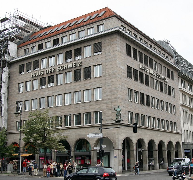 Berliner Architektur 1933-45: Haus der Schweiz. Diese Geschftshaus an der Ecke Friedrichstr / Unter den Linden war als reprsentatives Haus fr Versicherungen und Unternehmen aus der Schweiz (aber auch aus Dtl) gedacht. Der schweizer Architekt Meier-Appenzell bediente sich des sachlichen und monumentalen Baustils der 30er. Das Stahlskelett wurde mit Muschelkalk verkleidet, das EG ffnet sich durch Arkaden. Eine klare Fassadenstruktur wird durch die zu Bndern gefasste Fenster erreicht. Auch der Schriftzug besteht aus betont sachlichen Buchstaben. Einziges Schmuckelement ist die W.Tell Figur an der Ecke mit Armbrust und Pfeil.