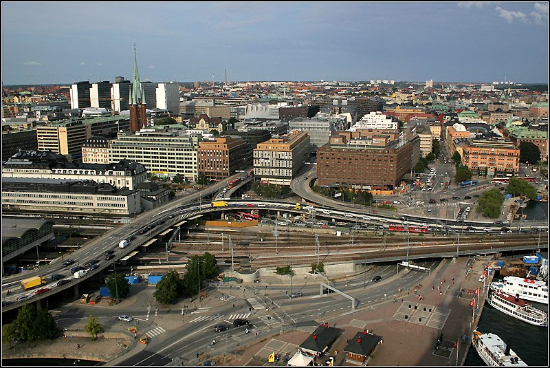 Blick vom Turm des Stadhuset auf Norrmal mit den fnf aufflligen Hochhusern in der Nhe des Sergels torg. Davor ist die Klar Kyrkan zu erkennen. Leider ist Stockholm an manchen Stellen, wir hier im Bereich Stadshuset, Bahnhof auch sehr vom Straenverkehr geprgt. Anstelle der heutige Unterfhrung rechts, gab es einst lediglich einen Bahnbergang. Zustzlich gibt es noch Hochstraen ber die Bahn. Zwischen den Husern in Bildmitte verschwinden die Autos im Klaratunneln, nach rechts fhren die Fahrbahnen parallel zur Eisenbahn kreuzungsfrei Mitten durch die Stadt (zwischen Riddarholmen und Gamla stan hindurch) bis in den Sden Stockholms. 20.8.2007 (Matthias)