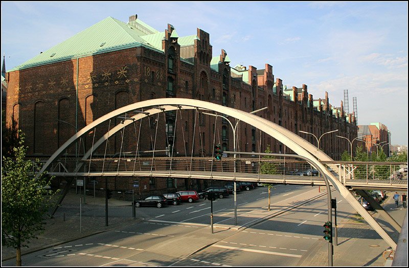 Da die Speicherstadt auerhalb der Sturmflutschutzbauten liegt, wurde fr den Fall eines Hochwassers eine weitere hherliegende Fugngerebene auf Stegen geschaffen. Dieser Steg verbindet die Neubauten auf der Sdseite des Sandtorkais mit der historischen Speicherstadt und ber einen weiteren Steg ber dem Binnenhafen auch mit der Hamburger Altstadt. Er befindet sich auf Hhe des Kehrwiedersteges. In der Gestaltung passen die neunen Stege zu den vorhandenen alten der Speicherstadt. Ein schnes Beispiel des Weiterbauens am Vorhanden mit zeitgemen Mitteln. Im Hintergrund rechts sind zwei Metallgittertrme zu erkennen, die wohl an einstmal an jener Stelle befindlichen Schonrnsteine erinnern sollen. 14.7.2007 (Matthias)