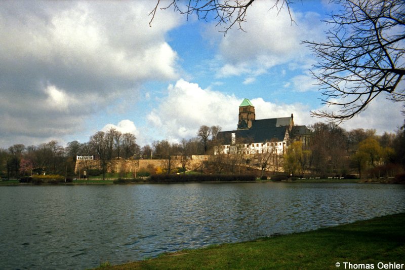 Die Schlosskirche zu Chemnitz thront weithin sichtbar ber dem Schlossteich. Es ist das historisch wertvollste Gebude der Stadt. Das weie Gebude vor der Kirche gehrt zum ehemaligen Benediktinerkloster, beherbergt heute das Schlossbergmuseum. Das Benediktinerkloster steht fr die Grndung der Stadt Chemnitz. Die Aufnahme entstand im Frhjahr 1996.