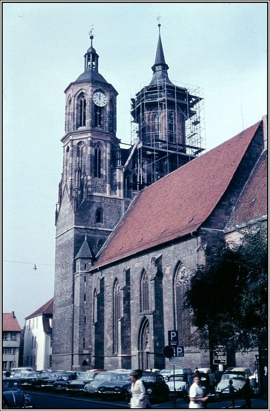 Die St. Johanniskirche in Gttingen, aufgenommen etwa Anfang der 60er Jahre des vergangenen Jahrhunderts. Das Bild ist der Scan eines Dias aus dem Archiv meines Vaters Alfred Schmidt. Die Kirche wurde von 1300 bis 1344 gebaut. Ihre Trme gehren zu den Wahrzeichen der Stadt. Meine Familie und ich haben lange Zeit nur wenige hundert Meter von dieser Kirche entfernt in der Johannisstrae gewohnt. Wie man sehen kann wurde zu dieser Zeit der Platz um die Kirche herum noch als Parkplatz genutzt. Einer der Trme wurde saniert. Im Rcken des Fotografen befindet sich das alte Rathaus der Stadt.