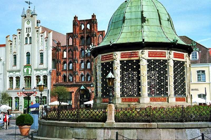 Die Wasserkunst auf dem Markt. Das Backsteingebude im Hintergrund ist der  Alte Schwede , Wismars ltester Profanbau aus dem 14. Jh. (September 2003)