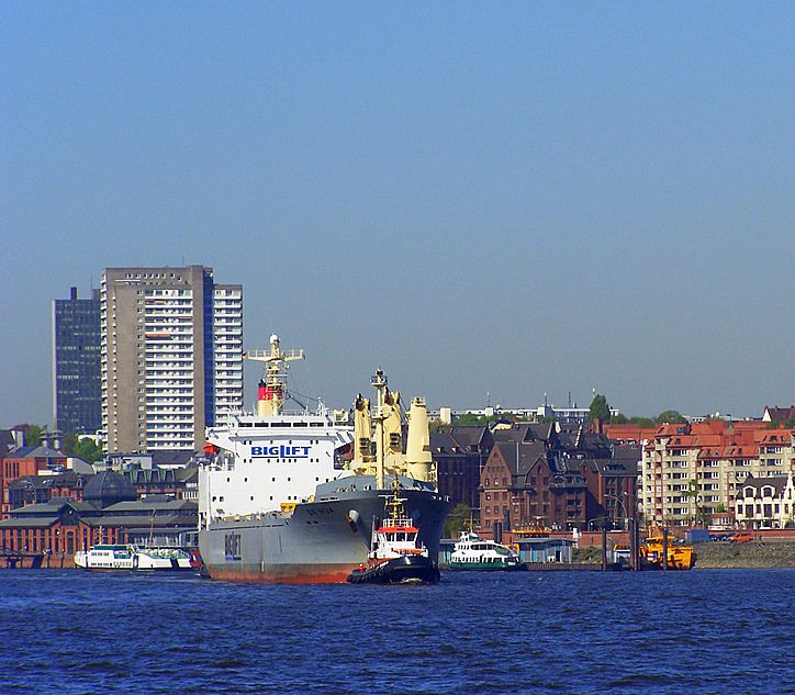 Ein Großes Containerschiff verlässt Hamburg meist nicht ohne Hilfe. Hier wird eines dieser  Riesen  von einem Kleinen Kutter aus dem Hafenbecken gezogen. Im Hintergrund ein schöner Blick auf Hamburg.