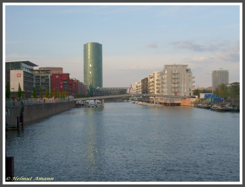 Frankfurt am Main, Blick vom Rotfederring in Richtung Osten. Auf dem Gelnde des ehemaligen Westhafens zwischen der Friedensbrcke und der Main-Neckar-Brcke entstand unter dem Motto Wohnen und Arbeiten am Flu ein modernes Stadtquartier mit Bros und Wohnungen, die teilweise auf Pfhlen im Wasser stehen und ber eigene Bootsanlegestege verfgen. Das architektonische Highlight ist der im Jahre 2003 fertiggestellte, 112 Meter hohe Westhafentower. Wegen seiner Form und der rautenartigen Fassadenstruktur, die dem typischen Apfelweinglas sehr hnelt, gilt der Westhafentower bei den Frankfurtern als das grte Ebbelweiglas der Welt (Aufnahme vom 03.05.2008).
