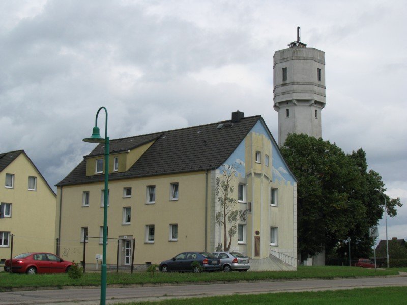 Grevesmhlen, Wohnblock, Ecke Wismarsche Strae, Ploggenseering mit Gemlde des Wasserturm, im Hintergrund Wasserturm an der Wismarschen Strae, 24.08.2008