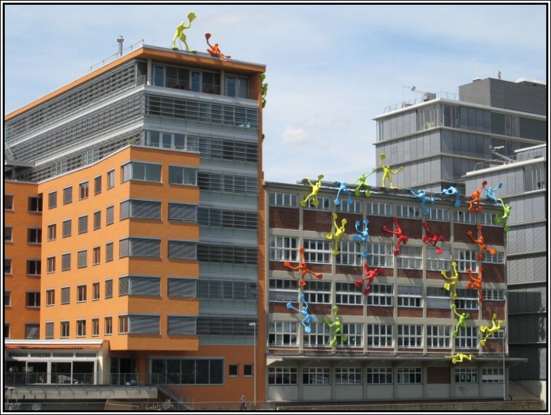 Hier sieht man ebenfalls Brogebude im Dsseldorfer Medienhafen. Eingerahmt von zwei Neubauten befindet sich in der Mitte ein umgebautes Speichergebude, das „Roggendorf-Haus“, fertiggestellt 2001. Bei den Figuren an der Fassade handelt es sich um das 29-teilige Figuren-Ensemble „Flossis“ der Knstlerin rosalie, eine dauerhafte Kunst-Installation. (08.07.2007)