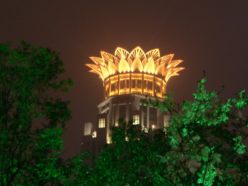 Hochhaus in Shanghai von einem Park aus betrachtet. Es war vielleicht 20 Uhr. Der Park ist grn beleuchtet. Einige Leute tanzten zu Musik, die sie mitgebracht hatten. Die Abendstimmung chinesischen Grostdten ist toll - es ist sehr viel los. April 2006