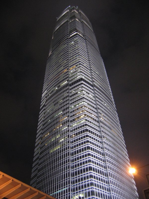 Hong Kong : Ein moderner Wolkenkratzer reckt sich aus den grellen Lichtern der Strassen in den dunklen Nachthimmel.