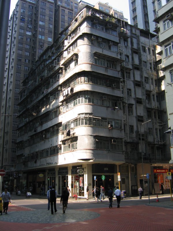 Hong Kong : Welch Tristesse! Noch ein Klassiker, auf dessen heruntergekommene Fassade nur noch ein paar Sonnenstrahlen fallen knnen, die das Haus zwischen den neuen hohen Gebuden noch trostloser erscheinen lassen. Eine chinesische Hausfrau mchte die Sonnenstrahlen ausnutzen und hat tatschlich etwas Wsche zum Trocknen herausgehngt. Mut zur Lcke! 