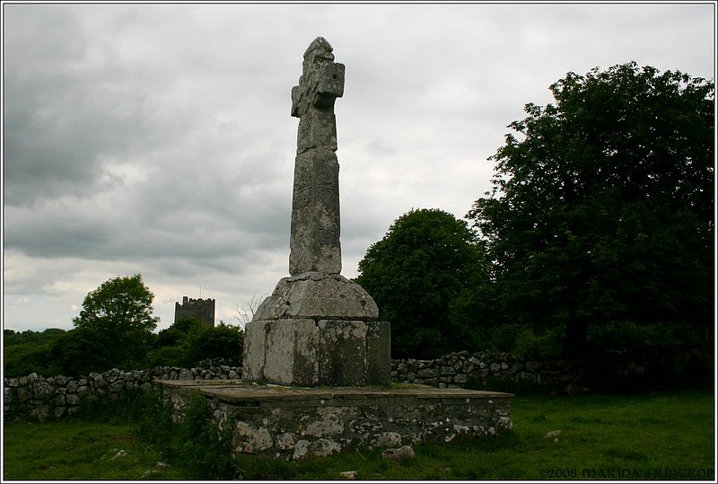 Impressionen vom Dysert o'Dea Archaeology Trail, Irland Co. Clare. Das St. Tola's Hochkreuz und dahinter das Dysert o' Dea Castle aus dem 15. Jahrhundert, das heute als Museum dient.