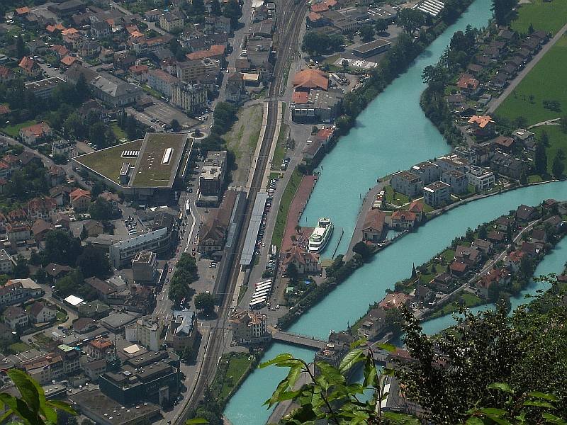 Interlaken im Berner Oberland, fotografiert vom Restaurant auf dem Harder Kulm (1322 Meter), dem Hausberg von Interlaken. Zentral im Bild der Bahnhof Interlaken-West mit seinen zwei Gleisen, rechts daneben der Hafen mit einem Ausflugsschiff. Der Hafen ist ber einen Kanal mit dem Thuner See verbunden. Die Aufnahme stammt vom 28.07.2008.