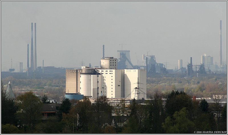 Mlheim an der Ruhr - Blick vom Bismarckturm. Am Bildrand links zeigt der Spitzturm den Standpunkt der Neuen Mitte Broich. In der Mitte die Aspera Bierbrauerei im Rhein-Ruhr-Hafen Mlheim (Entfernung 4 km). Direkt dahinter die Industrieanlagen von Duisburg, links sind die Kamine der Carbonario Kokerei in Duisburg Schwelgern zu sehen (Entfernung ca. 14 km). Hinter der Malzfabrik die Baustelle Block 10 des Kraftwerks Walsum (Entfernung ca. 17 km).