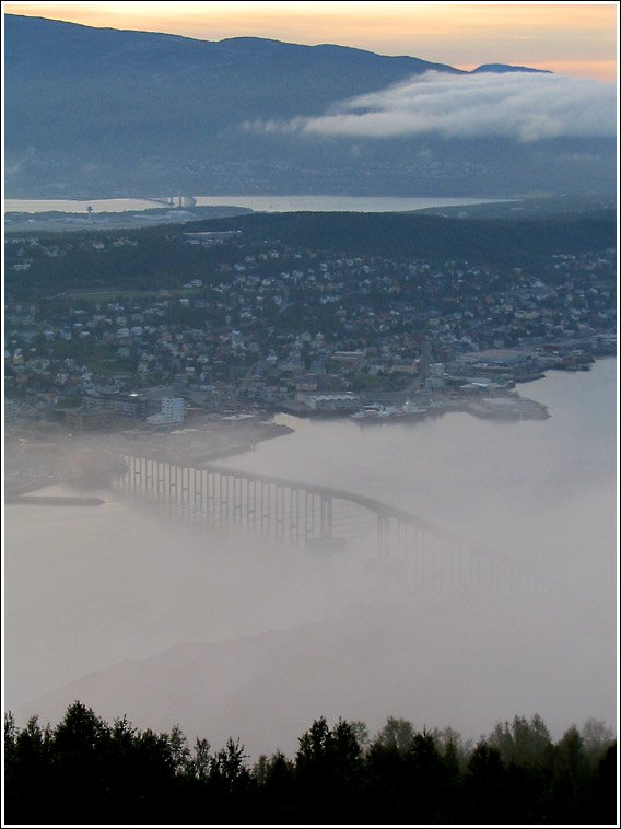 Neblige Ansicht von Troms: Vorne die bekannte Brcke, in der Mitte die Insel, auf der der grte Teil der bebauten Stadt liegt. Dahinter die Insel Kvalya, zu der eine weitere im Bild erkennbare Brcke fhrt. 10.8.2006 (Jonas)