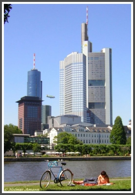 Summer in the city: Das Flussufer ist fr viele Bewohner von Frankfurt am Main im Sommer ein Ort zum Entspannen mitten in der Stadt. Am 15.07.2005 tat das auch dieser Mensch vor der Hochhauskulisse des Japan Centers und dem Main Tower im Bild links sowie dem mit 259 Meter struktureller Hhe zweithchsten Wolkenkratzer Europas, dem Commerzbank Tower. Dazwischen flog gerade ein Werbeluftschiff.