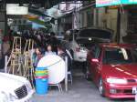 Hong Kong : Raum ist in der kleinsten Htte! Die jungen Leute sitzen an den Tischen eines kleinen Restaurants in direkter Nhe neben einer Autowerkstatt.