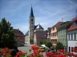 Blick von der Rathaustreppe ber den Marktplatz der frnkischen Kleinstadt Aub im Landkreis Wrzburg auf die Stadtpfarrkirche  Maria-Himmelfahrt  in der sich die  Kreuzigungsgruppe  von Tilman