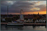 Blick vom Schiff auf Warnemnde: Zwischen Warnow und Bahnhof Warnemnde leuchtet ein Riesenrad im Abendlicht.