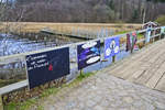 Kunstdrcke des Flensburger Knstlers Christian Ristau hngt an das Gelnder der Holzbrcke zwischen Wassersleben und dem Kollunder Wald auf dnischer Seite der