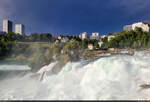 Umgeben von Hochhusern, flieen gewaltige Wassermassen den Rheinfall in Neuhausen (CH) hinunter.