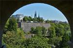 Blick von der Fugngerpassage durch einen Brckenbogen unter der Neuen Brcke in der Stadt Luxemburg, auf die Kathedrale und das Kriegsdenkmal mit der „Gle