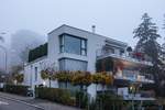 Ein modernes Haus im vorgrund und das Waldhaus Dolder im Hintergrund in Nebel  gekleidet .