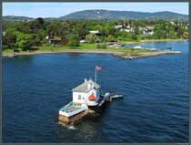 Die winzige Insel Dyna an der Einfahrt zum Hafen Oslo wurde 1874 mit einem Leuchtfeuer bebaut. Heute dient das Gebude als Restaurant. Dahinter befindet sich die zu Oslo gehrende Halbinsel Bygdy. Im Hintergrund ist die Skischanze Holmenkollbakken zu erkennen. (Oslo, 28.05.2023)
