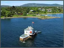 Die winzige Insel Dyna an der Einfahrt zum Hafen Oslo wurde 1874 mit einem Leuchtfeuer bebaut. Heute dient das Gebude als Restaurant. Dahinter befindet sich die zu Oslo gehrende Halbinsel Bygdy. Im Hintergrund ist die Skischanze Holmenkollbakken zu erkennen. (Oslo, 28.05.2023)
