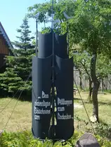  Den ehemaligen Bewohnern von Pillkoppen zum Gedenken 
Dieses Denkmal steht in einem Vorgarten in Pillkoppen.
Pillkoppen ist ein kleines Dorf auf der Kurischen Nehrung. (russischer Teil). Das Denkmal stellt das Segel eines Schiffes dar, Pillkoppen war einst ein ostpreu�isches Fischerdorf.