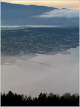 Neblige Ansicht von Troms: Vorne die bekannte Brcke, in der Mitte die Insel, auf der der grte Teil der bebauten Stadt liegt. Dahinter die Insel Kvalya, zu der eine weitere im Bild erkennbare Brcke fhrt. 10.8.2006 (Jonas)