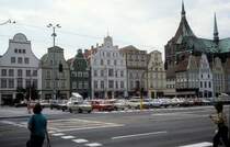 Rostock am 1. Juli 1990: Ernst-Thlmann-Platz. - In den Jahren 1952 - 1991 hiess Neuer Markt, der historische Markt der Rostocker Mittelstadt, 'Ernst-Thlmann-Platz'. Nach dem Zweiten Weltkrieg waren 90 Prozent der Huser hier zerstrt, die Giebelhuser an der Westseite des Marktes - die Huser auf dem Foto - wurden aber neu errichtet. Rechts ist ein Teil der Marienkirche zu sehen.